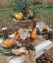 a vintage Thanksgiving tablescape with a large urn with greenery and veggies, a burlap table runner and some  pumpkins and berries on the table