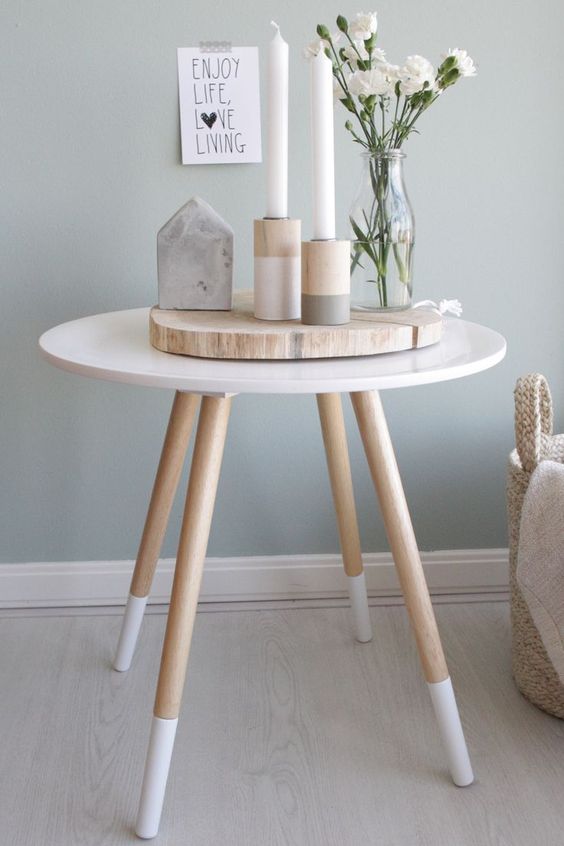 Cute spring Scandi decor with a wood slice, wooden color block candleholders and candles, a stone house shaped piece and white blooms in a vase