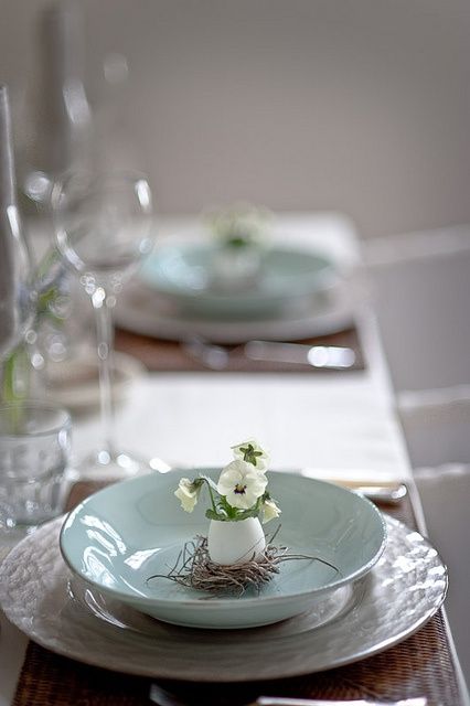 a spring place setting with a mother of pearl and blue plate and some pansies in an egg shell for a Nordic spring touch