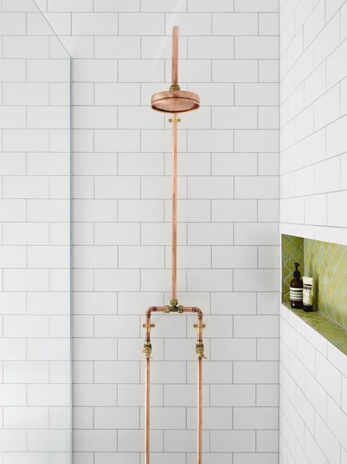 A modern shower space clad with white subway tiles, with a grene niche and gold exposed pipes of the shower itself is an eye catchy space