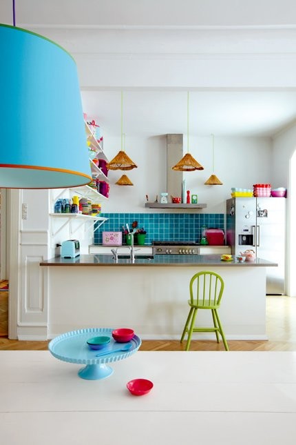 a playful kitchen with white cabinetry, stainless steel appliances, a bold blue backsplash and lamps and some colorful touches is fun