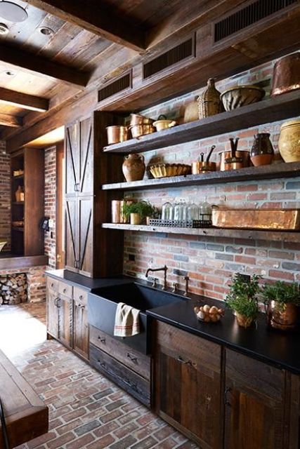 A vintage rustic dark stained kitchen with rough wooden cabinets, black countertops, open shelves, a red brick backsplash and vintage appliances is amazing