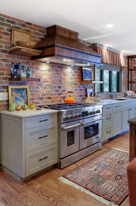 a grey kitchen with shaker style cabinets, grey countertops, a red brick backsplash, a vintage metal hood, open shelves and lots of natural light