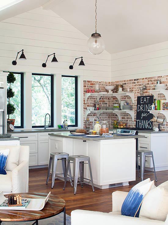 a modern white kitchen with white shaker style cabinets, grey stone countertops, open shelving and a red brick backsplash, black sconces and pendant lamps