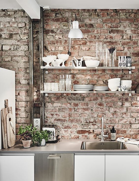 a clean white Scandinavian kitchen with sleek cabinets, concrete countertops and a rough red brick backsplash that adds interest and chic to the space