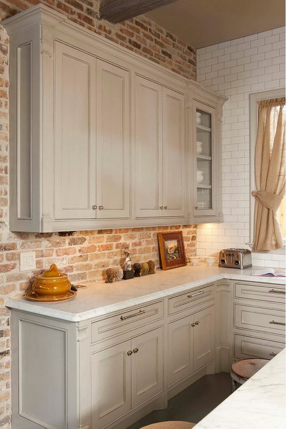 an elegant dove grey kitchen with shaker style cabinets, white countertops, a red brick backsplash, neutral curtains is a lovely idea for an eclectic home