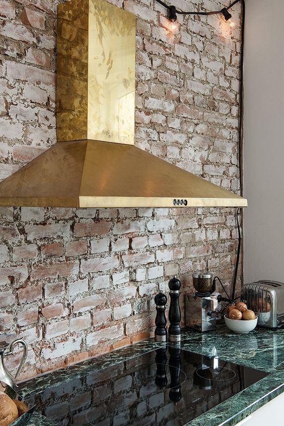 a whitewashed brick backsplash balances out a shiny gold hood and a green stone countertop and gives a historical feel to the space