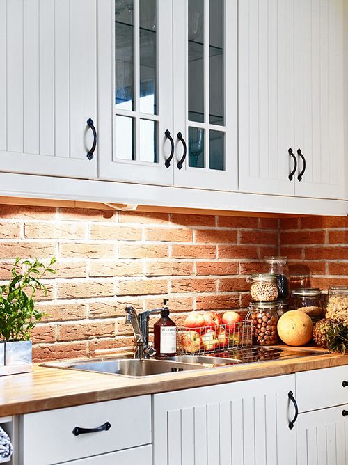 A white farmhouse kitchen with beadboard cabinets, black handles, a red brick backsplash and built in lights is a very cozy space to be