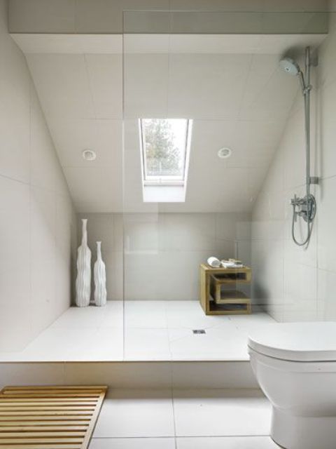 a small contemporary attic bathroom with large scale creamy tiles and a skylight in the shower