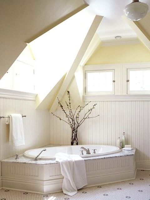 a creamy bathroom with skylights, a built-in bathtub and a branch arrangement in a vase