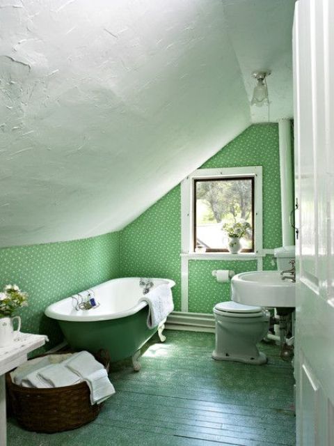 a grene attic bathroom done with wallpaper, a green wall and a green clawfoot tub plsu a basket for storage