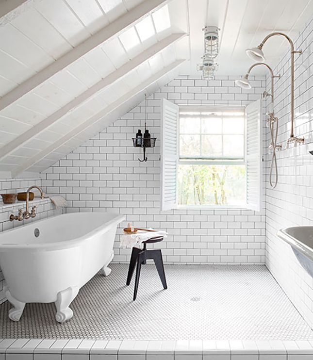 an airy white bathroom with subway and penny tiles and black grout, a clawfoot tub and a black stool