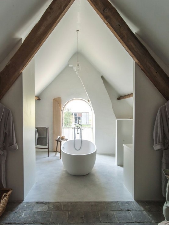 a neutral attic bathroom with a large arched window, a tub and some furniture for storage