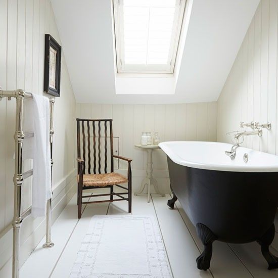 a neutral vintage attic bathroom with a skylight and a black clawfoot tub, a vintage chair