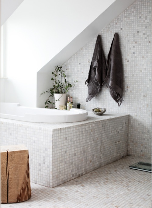 a neutral attic bathroom with a sunken tub, small scale tiles and a tree stump side table