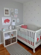 a cozy tiny nursery with a grey wall, a polka dot accent wall, a white crib, a storage unit and a small and cute gallery wall