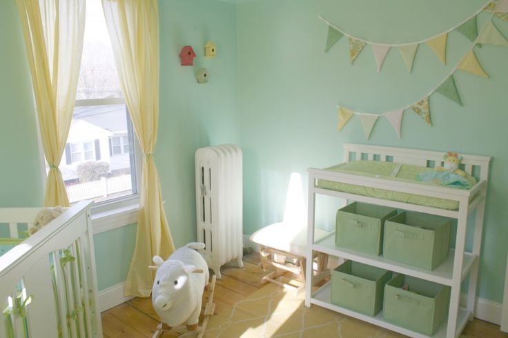A small mint colored nursery with white furniture, yellow curtains, buntings and toys, baskets and boxes is a great space