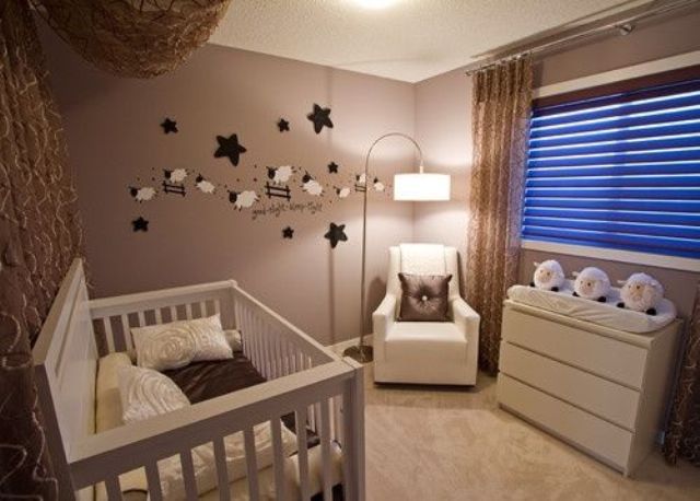 A tiny taupe nursery with a white crib, a white chair and dresser, a funny gallery wall and some lights