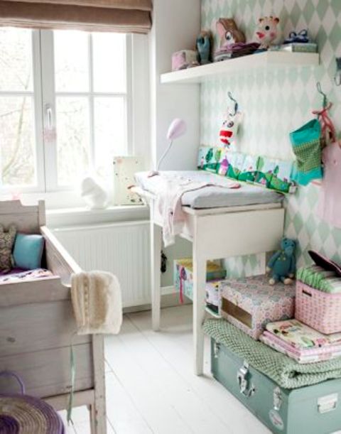 a vintage Scandinavian nursery with a whitewashed wooden crib, a changing table, a mint-colored suitcase and a shelf plus an accent wall done with wallpaper