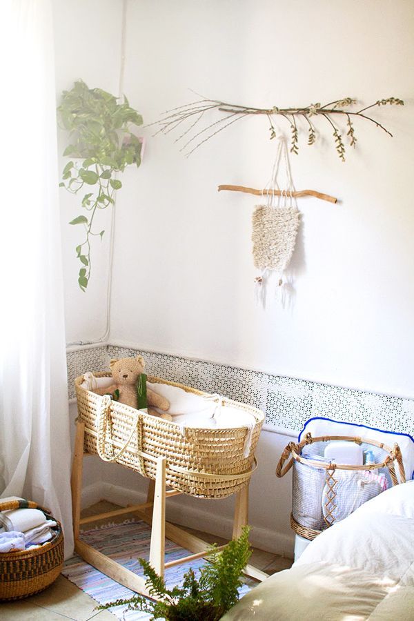 A tiny nursery with a little basket style crib, a sofa, a basket for textiles, greenery and branches is amazing for a boho home