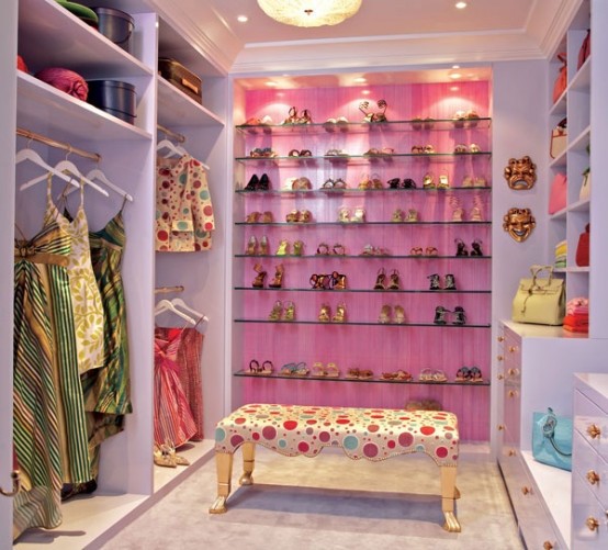 a bright and cool feminine closet with a pink accent wall and glass shoe shelves, lilac open storage units and a pretty polka dot bench is amazing