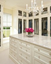 a pretty neutral walk-in closet with glass wardrobes and an oversized cabinet with lots of drawers for storing smaller stuff and accessories