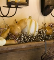 a mantel decorated with pumpkins and gourds plus blooms looks all-natural and very fall-like