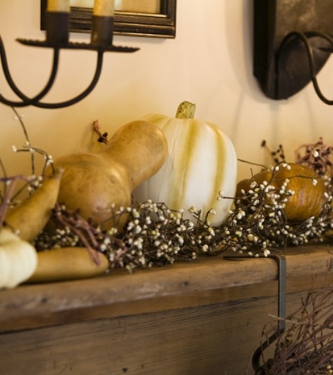 A mantel decorated with pumpkins and gourds plus blooms looks all natural and very fall like