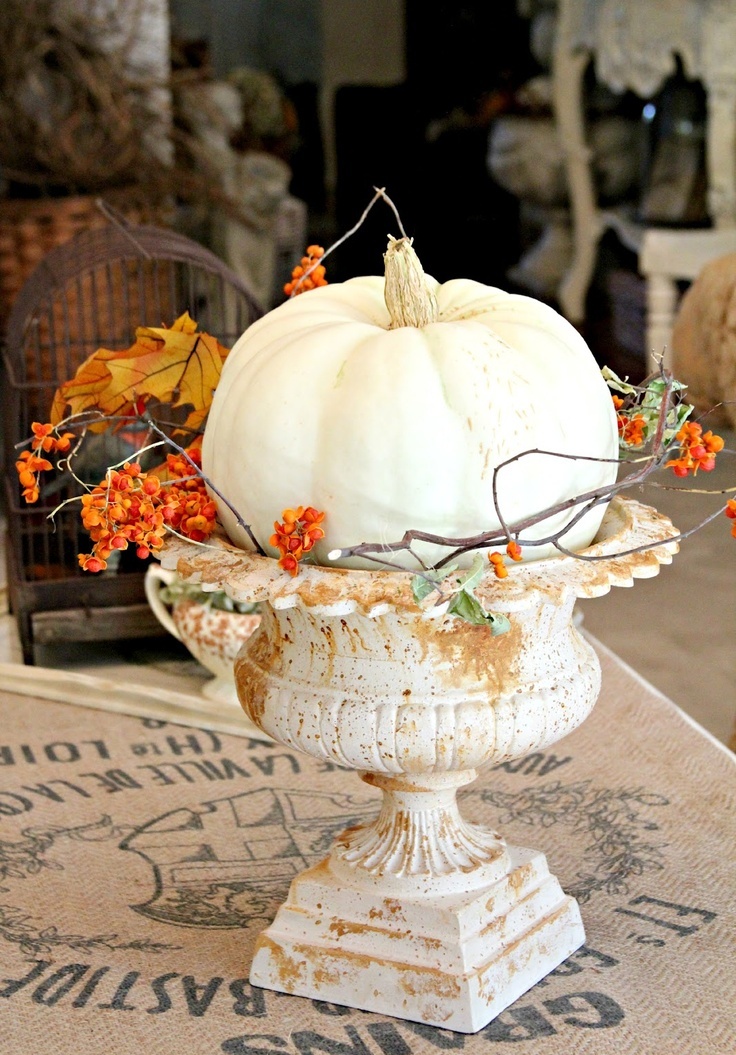 A vintage urn with blooming branches and a large white pumpkin is a chic fall decoration for outdoors