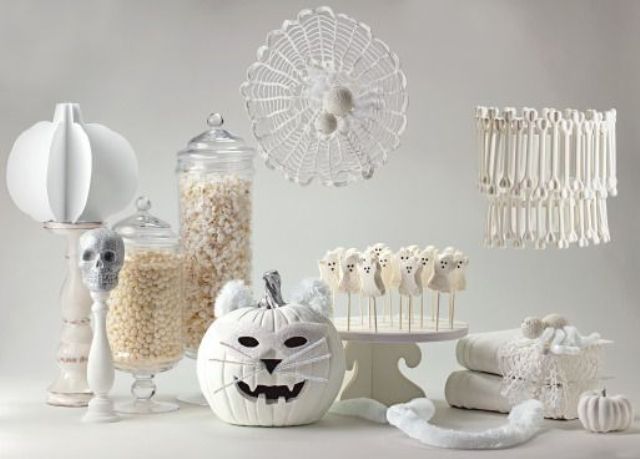 A white Halloween sweets table with a skull, a jack o lantern, various candies, sweets and sugar bones
