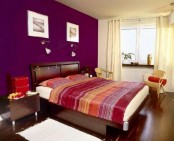 a colorful bedroom with a purple accent wall, dark stained furniture, bright bedding, sconces and artworks is a perfect warm-colored bedroom