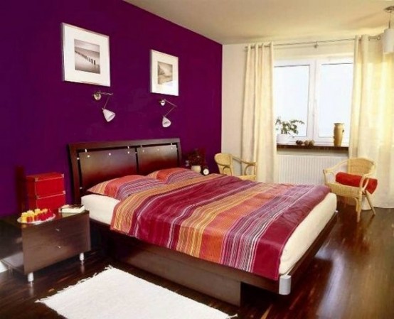 a colorful bedroom with a purple accent wall, dark stained furniture, bright bedding, sconces and artworks is a perfect warm-colored bedroom
