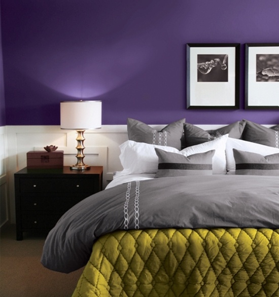 a bold purple bedroom with white paneling, grey and white bedding, a mustard blanket, dark stained furniture and chic artworks