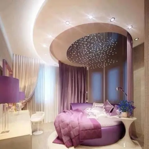 a warm tan and purple bedroom with a round bed, a rounded ceiling with lights, purple bedding and table lamps