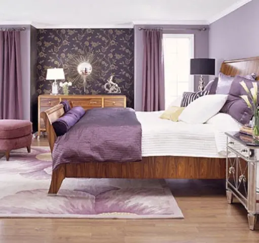 purple and lavender bedroom with printed wallpaper, stained wooden furniture, table lamps, a sunburst mirror and some purple textiles