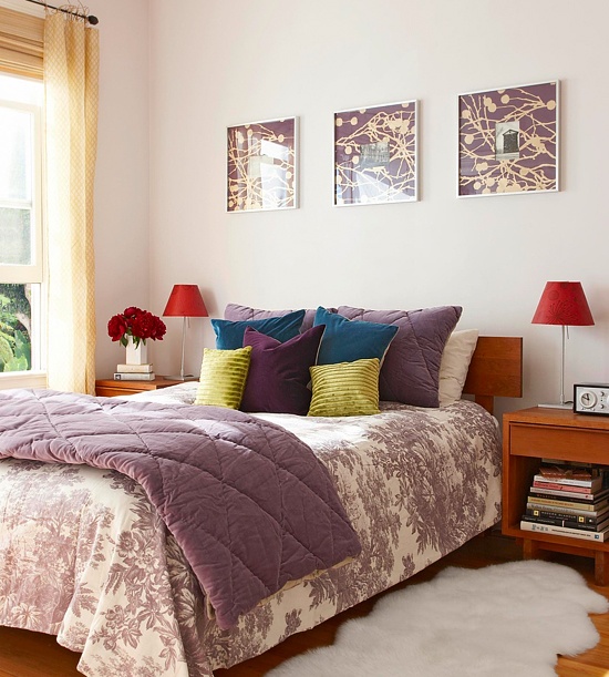 A colorful bedroom with mid century modern wooden furniture, bright bedding and pillows, purple bedding and artworks