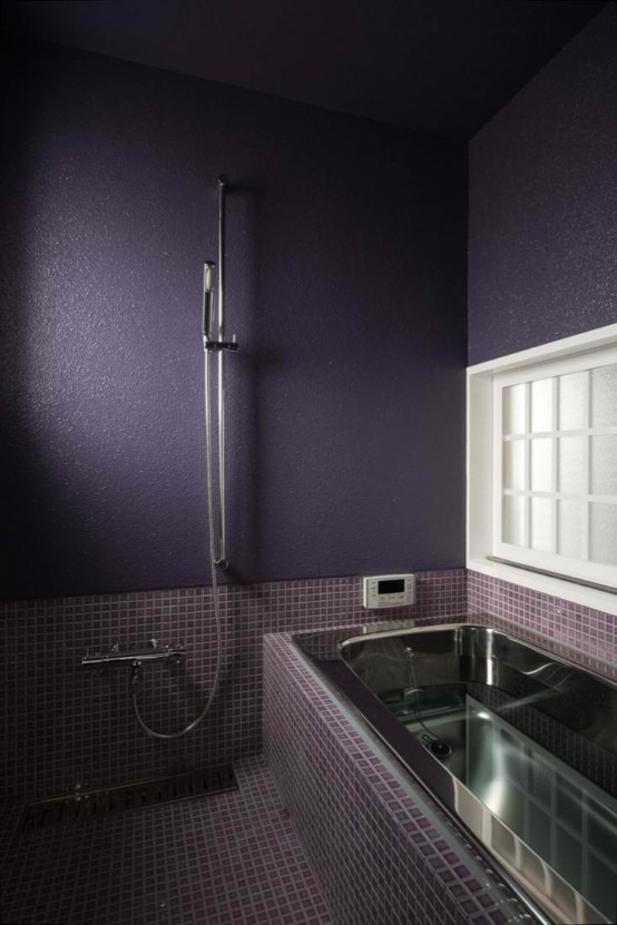 a moody bathroom done in deep purple, matte purple walls, fuchsia and purple tiles and a metal bathtub