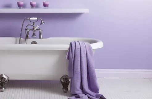 a cozy lavender infused bathroom with a white vintage tub and a white tile floor