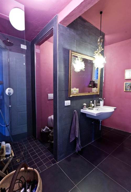 a bold mauve and purple bathroom with various types of tiles, elegant lighting and a gallery wall
