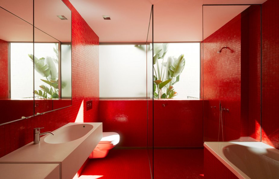 A minimalist red bathroom done with a large window and white appliances   a sink and a tub