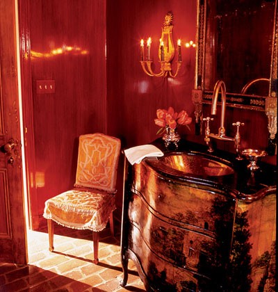 a refined red and gold bathroom with a vintage feel, a chic vanity, a wall sconce and a vintage chair