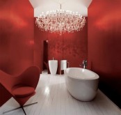 a refined red bathroom with a free-standing sink and tub, a chic red chair and a statement crystal chandelier