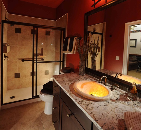 a modern bathroom with burgundy walls, with neutral stone and neutral tiles in the shower and some lights