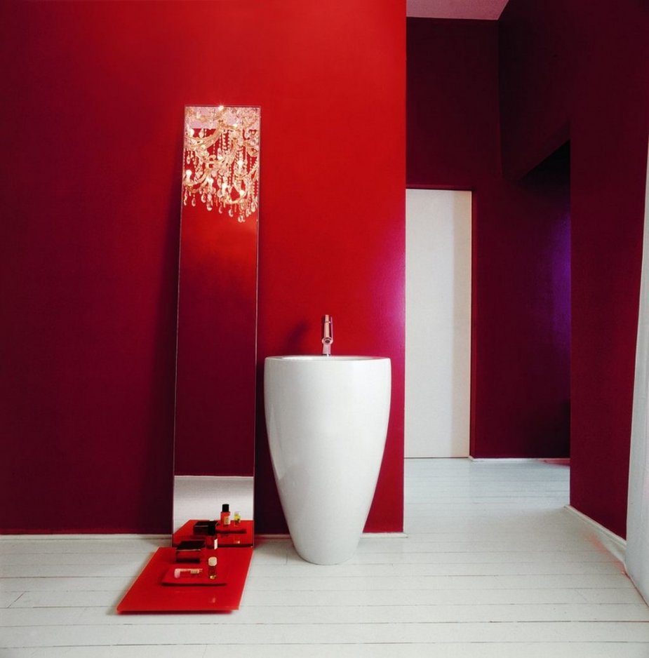 A unique minimalist bathroom in red, with a free standing sink, a mirror with a shelf and a white floor