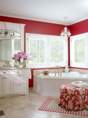 a traditional red bathroom with white furniture, appliances and a red ottoman plus a crystal chandelier