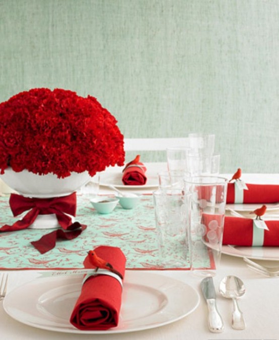 a red, mint green and white Christmas tablescape with a red rose centerpiece in a bowl with a red bow, a mint green table runner, white porcelain and bold red napkins