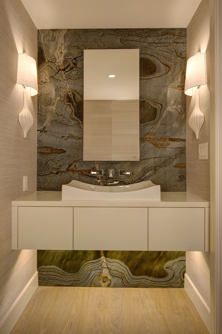 A neutral bathroom with a grey onyx accent wall, a built in vanity and a sink, wall sconces looks luxurious and chic
