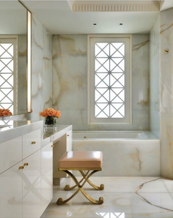 a luxurious modern bathroom fully clad with white onyx panels, with a large white vanity, a pink stool and touches of gold is a lovely idea