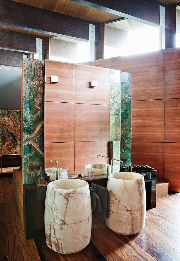 A catchy contemporary bathroom done with stained wood panels, with bold green onyx accents and white onyx free standing sinks that make the space ultimate