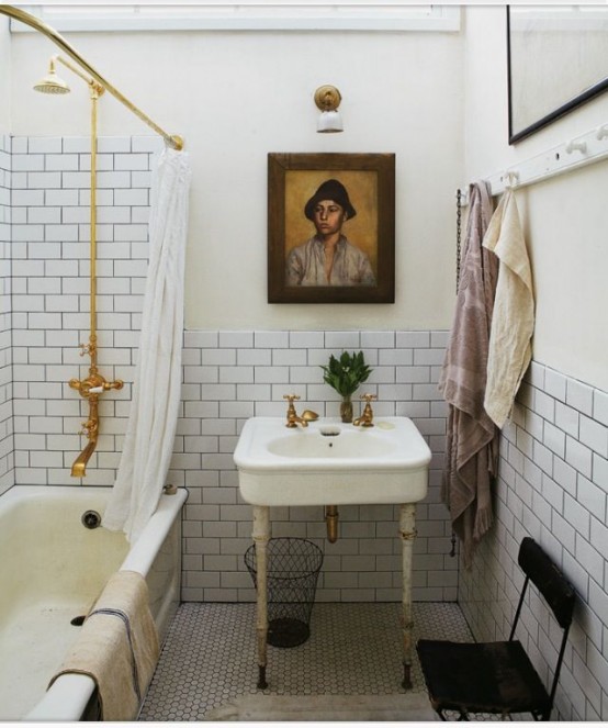 a neutral bathroom with white subway tiles, a neutral bathtub, a free-standing sink, a black chair and gold fixtures is amazing